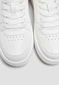 Weiße Sneakers mit glattem Lederobermaterial, runder Zehenpartie, durchbrochenen Details, flachen Schnürsenkeln und kontrastierender Gummisohle.