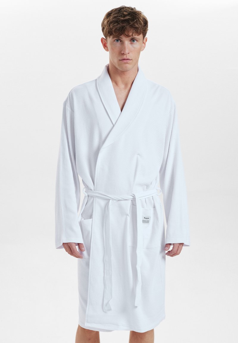 Bata de baño blanca de algodón con un patrón texturizado, diseño envolvente, mangas largas y cinturón de lazo en la cintura. Cuenta con bolsillos a los lados.