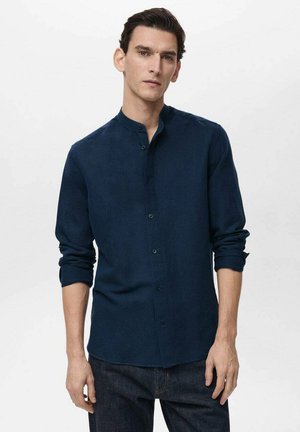 Marineblå skjorte med knapper lavet af blødt stof, med stående krave, lange ærmer og optrukne manchetter, parret med mørke denimjeans.