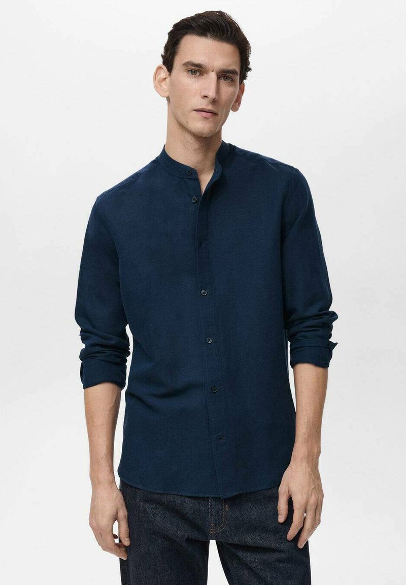 Navy blue button-up shirt made of soft fabric, with a stand collar, long sleeves, and rolled cuffs, paired with dark denim jeans.