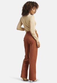 Brown suede high-waisted pants with wide legs, paired with a beige long-sleeve top. Smooth texture and a fitted silhouette.