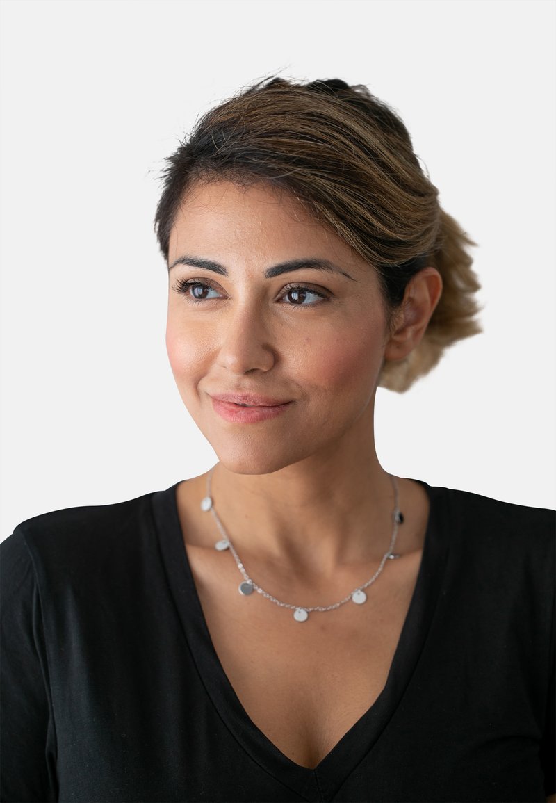 Collana in argento con pendenti circolari, caratterizzata da una finitura metallica liscia. Indossata con una camicia nera a scollo a V.