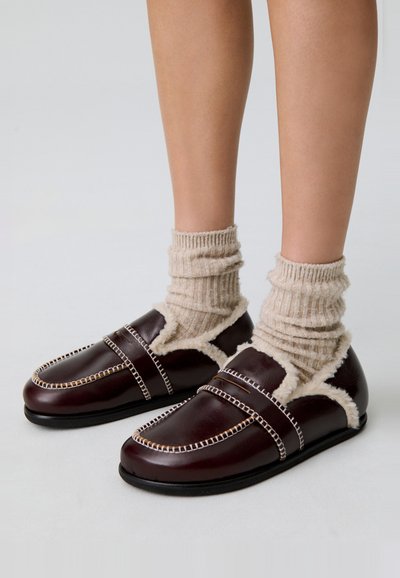 Scarpe in pelle marrone con fodera in shearling, dotate di cuciture bianche a contrasto e design a punta chiusa. Abbinate a calze a coste beige.