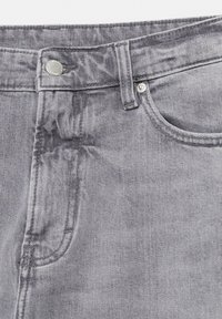 Detailní záběr šedých džínů z denimu zobrazující pas, knoflík, poutko na opasek a přední kapsu.