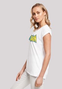 White cotton t-shirt featuring a bold yellow and blue "HERO" graphic. Short sleeves and relaxed fit with rolled cuffs.