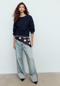 Maglione lavorato a maglia navy, vestibilità oversize. Vestito a portafoglio nero a pois e jeans larghi azzurri con orli sfrangiati. Scarpe con tacco nero e punta appuntita.