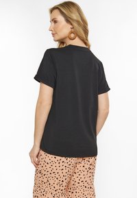 Sort kortærmet t-shirt med en afslappet pasform, der har rullede ærmer og en glat tekstur. Kombineret med prikket bukser i pink mønster.