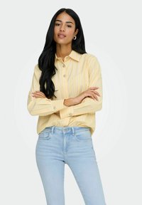 Chemise jaune clair à manches longues avec des rayures blanches verticales, design à col et fermeture par boutons, associée à un jean taille haute bleu clair.