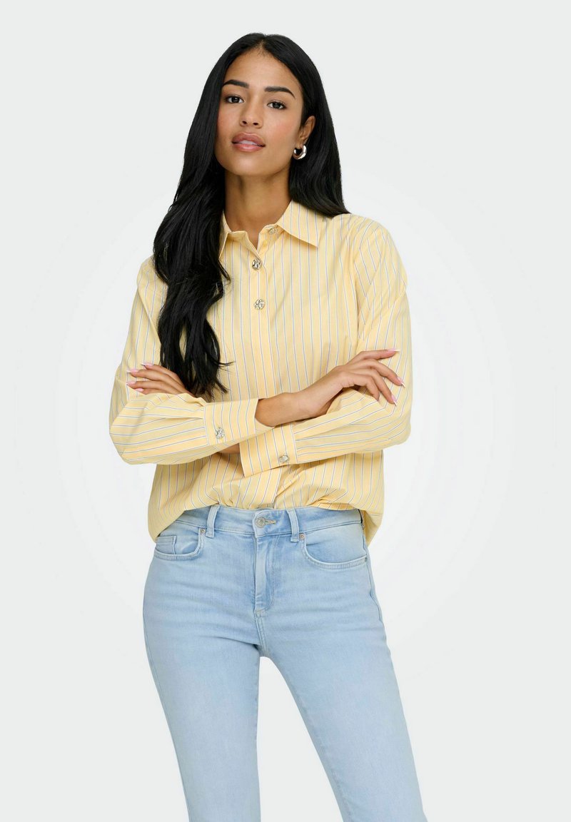 Chemise jaune clair à manches longues avec des rayures blanches verticales, design à col et fermeture par boutons, associée à un jean taille haute bleu clair.
