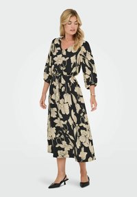 Crna haljina s bež cvjetnim uzorkom, V-izrezom, rukavima do tri četvrtine, s remenom na struku i lepršavim siluetom. Crne slingback potpetice.
