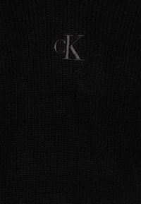 Czarny sweter z dzianiny o teksturowej powierzchni, z wyszywanym szarym logo "cK" z przodu. Prosty i zorganizowany design.