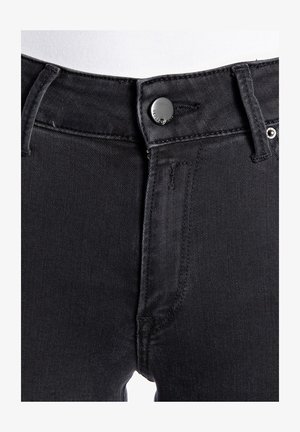 Mustad teksad, millel on keha lähedane lõige, klassikaline viie tasku stiil, tugev nupp ja vöörihma aasadega vööl.