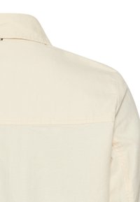 Back view of a beige long-sleeve shirt with a collar and visible seam across the upper back and shoulder area.