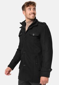 Abrigo de mezcla de lana negro con un diseño de doble botonadura, grandes botones, hombreras, bolsillos laterales y un cuello alto. Textura suave.