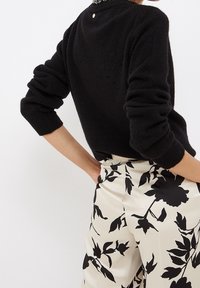 Zwarte wollen trui met een ronde halslijn en geribbelde manchetten, gecombineerd met high-waist crème broeken met een zwarte bloemenprint.