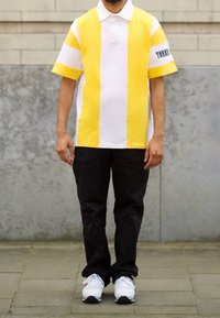 Yellow and white striped short-sleeve polo shirt with a collar, worn with black pants and white sneakers. "TOMMY" text on the sleeve.