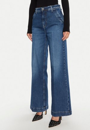 Jeans di jeans blu a gamba larga con vita alta, cinque tasche e dettagli di cuciture visibili. Abbinati a tacchi neri con punta appuntita.