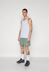 Ljusblå ärmlös linne med nätstruktur kombinerad med gröna träningsshorts med en vit Nike-logotyp. Svarta sneakers och vita strumpor.