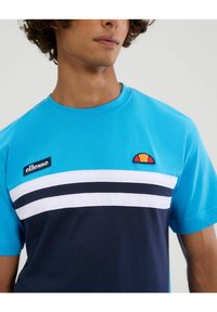 T-shirt in cotone blu con collo rotondo, caratterizzata da righe orizzontali bianche e navy, e un logo Ellesse ricamato in un design circolare.