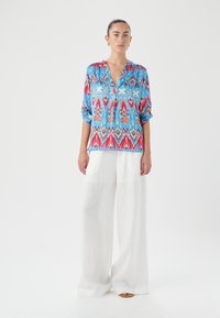 Blusa multicolore con motivo e scollatura a V, vestibilità comoda e maniche 3/4, abbinata a pantaloni bianchi in lino a gamba larga.