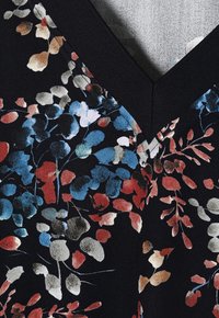 Kwiatowa bluzka na czarnym tle, z kolorowymi płatkami w odcieniach niebieskiego, czerwonego i kremowego. Teksturowana tkanina i dekolt w kształcie litery V.