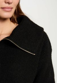 Black knit sweater with a textured surface, featuring a wide collar and a gold-tone zipper along the neckline.