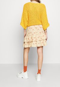 Pullover giallo a maglia con maniche larghe abbinato a una gonna a balze lunghezza ginocchio con un motivo floreale in beige e arancione. Sneakers bianche.