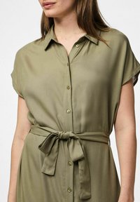 Olivgrön skjortklänning i lätt tyg, med krage, korta ärmar, knäppning framtill och ett knytbälte vid midjan.