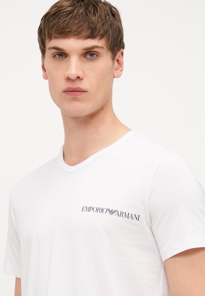 White short-sleeve V-neck T-shirt made of smooth fabric, featuring a small navy logo on the left chest. Simple design with no patterns.