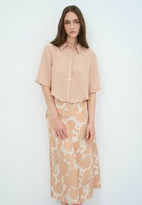 Kurze, hellrosa, cropped Bluse mit Knöpfen, kombiniert mit einem langen, gemusterten Rock, der abstrakte Formen in Beige und Creme zeigt.