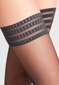 Czarne, przezroczyste, wysokie pończochy do ud z teksturowanymi gumkami, zdobionymi paskowanym wzorem u góry. Gładkie wykończenie, dopasowany krój.