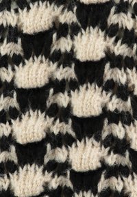 Nahaufnahme von schwarzem und beigem Garn, das in einem strukturierten Zickzack- und Ovalmuster gestrickt ist, mit sichtbaren Fasern und Stichen.