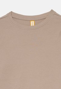 Light brown ribbed cotton t-shirt with a crew neck and a vertical textured pattern. Features a small yellow tag with the brand name.