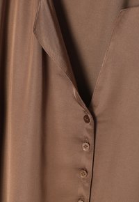 Tissu satin marron avec un col à revers et une rangée verticale de petits boutons ronds sur le devant.