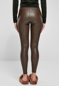 Bruna imitationläder leggings med en glänsande finish, åtsittande hela vägen, i kombination med fluffiga, bruna tofflor som liknar skor.