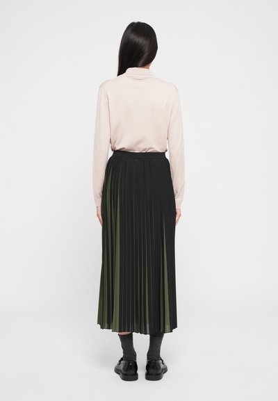 Black and olive green pleated skirt with an elastic waistband, paired with a light pink top and dark gray socks, worn with black shoes.