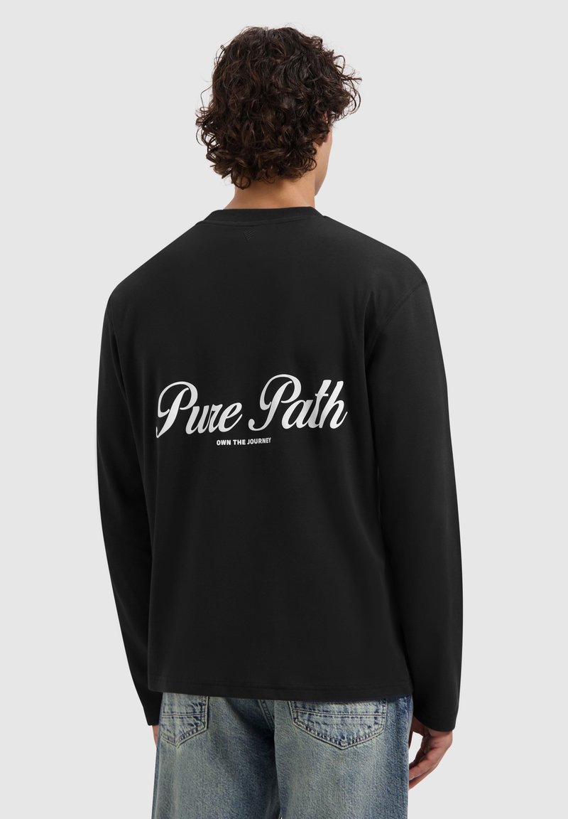 Zwarte longsleeve shirt met witte tekst "Pure Path" en "OWN THE JOURNEY" op de achterkant. De stof lijkt zacht en heeft een relaxte pasvorm.