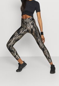 Leggings con motivo nero e oro, vita alta e superficie testurizzata. Abbinati a una maglietta nera a maniche corte e scarpe nere.