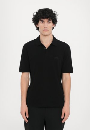 Polo noir avec un col, des manches courtes et un logo discret sur la poitrine. Tissu doux et lisse avec une coupe classique.