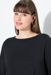 Maglietta nera a maniche lunghe con scollatura rotonda, realizzata in tessuto morbido. Presenta un design semplice e minimalista e una vestibilità comoda.