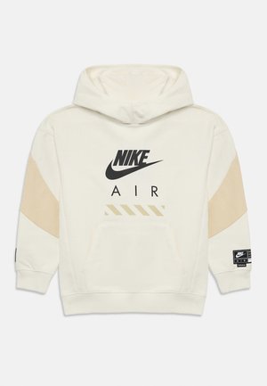 Hoodie Nike, couleur crème, avec un logo et un texte noirs. Présente des accents beiges sur les manches, une poche kangourou et une étiquette en tissu sur la manche.