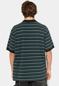 Camisa polo a rayas en negro, con rayas horizontales en azul y verde. Mangas cortas y un collar clásico con un corte relajado.
