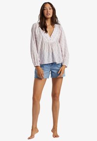 Långärmad, ljusrosa blus med blommönster, V-ringning och puffärmar, i kombination med denimshorts med fransad fåll.