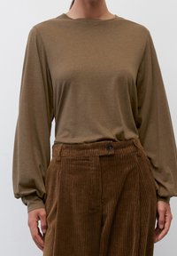 Braunes Langarmoberteil mit rundem Ausschnitt, kombiniert mit braunen Cordhosen, die auffällige vertikale Rillen und einen Knopfverschluss aufweisen.