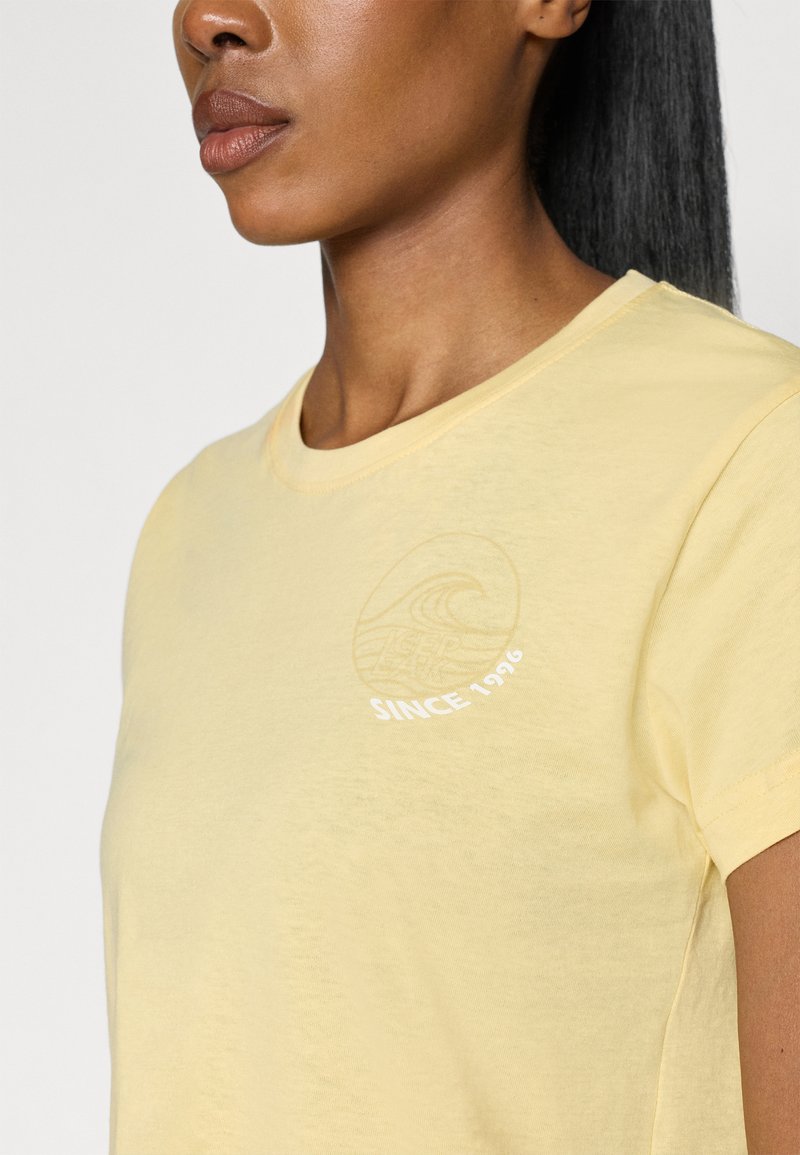 Jasnożółta bawełniana koszulka z okrągłym dekoltem, krótkimi rękawami i haftowanym wzorem fali z napisem "SINCE 1926" na klatce piersiowej.
