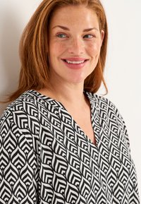 Black and white patterned blouse featuring a V-neck design, with a geometric leaf print and smooth fabric texture.