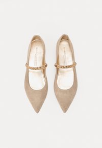 Ballerines en suédine beige à bout pointu avec une sangle métallique ornée de clous ronds. Doublure intérieure lisse, design minimaliste.