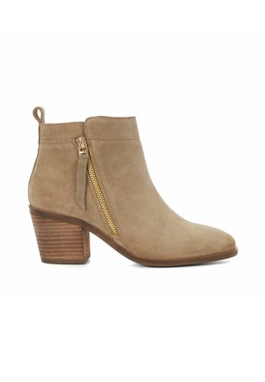 Botte de cheville en suède beige avec un bout pointu, fermeture éclair latérale dorée et talon en bois empilé. Texture lisse et design minimaliste.