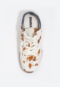 Zapatilla blanca con patrón marrón moteado, parte superior texturizada, puntera redonda y cordones beige. En el interior cuenta con una plantilla de marca y forro azul.