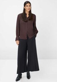 Chemisier marron à boutons avec une coupe décontractée, associé à un pantalon large noir et des bottines noires. Tissu lisse et manches longues.